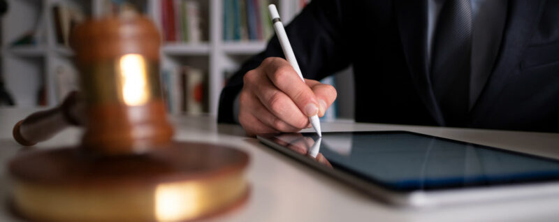 A close up of a judges gavel and a person drawing on a ipad with an apple pen